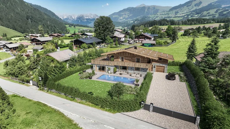 Luftaufnahme eines luxuriösen Chalets mit Pool und Garten in einer malerischen Berglandschaft im Sommer.