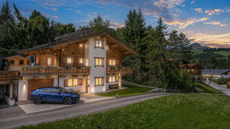 Charmantes Chalet-Haus in den Alpen mit Holzfassade und gepflegtem Vorgarten bei Sonnenuntergang.