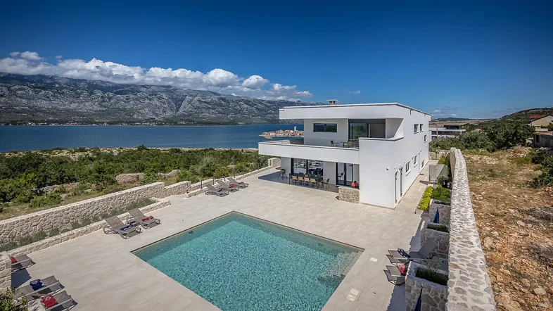 Moderne Villa mit großem Poolbereich, Sonnenliegen und atemberaubendem Meer- und Bergblick.