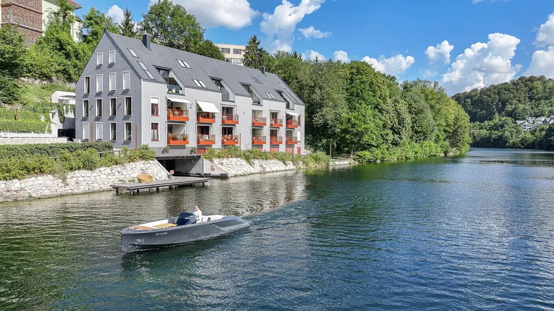 Modernes Apartmentgebäude direkt am Wasser mit Balkonen und Blick auf die umliegende Natur.