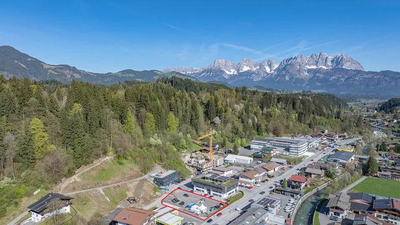 Luftaufnahme einer ländlichen Ortschaft mit Bergen im Hintergrund und einem rot umrandeten Grundstück.