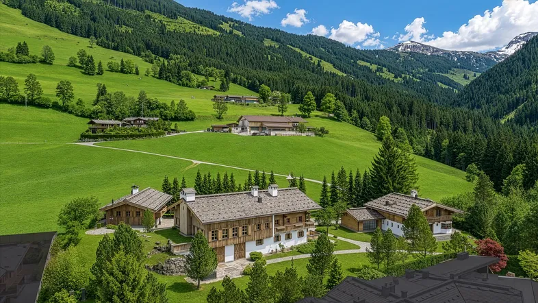 Malerische Luftaufnahme von mehreren Chalets in einer grünen Berglandschaft unter blauem Himmel.