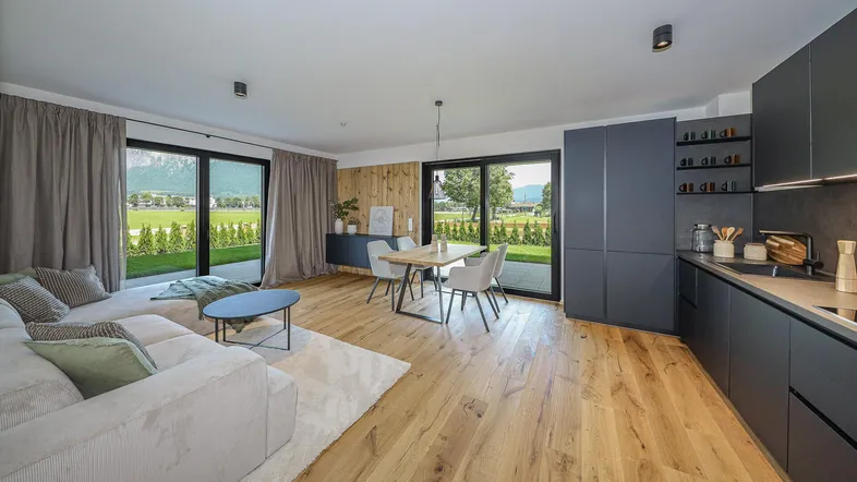 Heller offener Wohn- und Essbereich mit moderner Küche, Holzboden und Zugang zur Terrasse mit Bergblick.