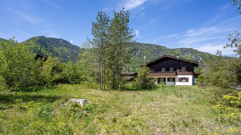 Traditionelles Haus in ländlicher Umgebung mit Bergen im Hintergrund und viel Grünfläche.
