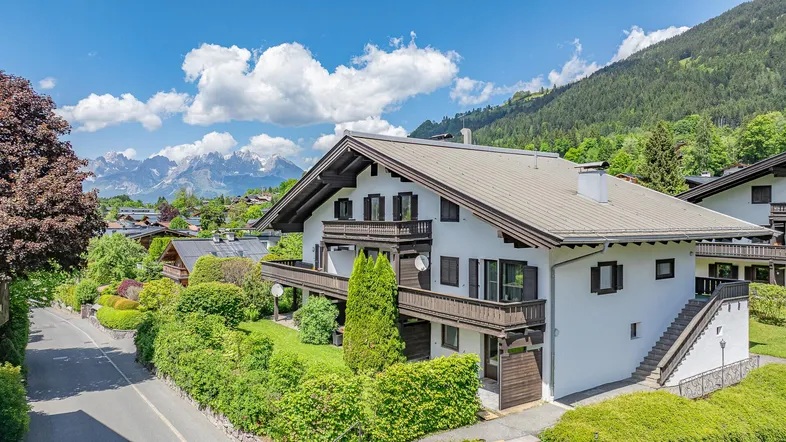 Traditionelles Haus im Alpenstil mit Balkonen und Bergblick unter blauem Himmel.