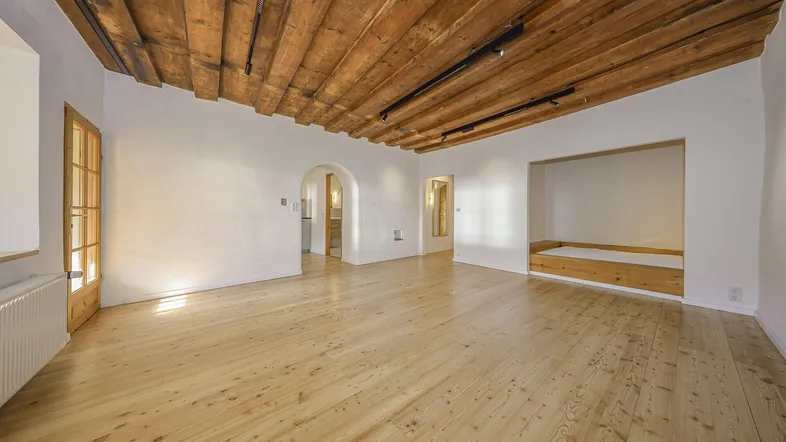 Geräumiges Wohnzimmer mit Holzbalkendecke, hellem Holzboden und integrierter Schlafnische.