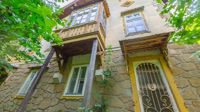 Historische Fassade eines Gebäudes mit dekorativem Holzbalkon und steinverkleidetem Sockelbereich.