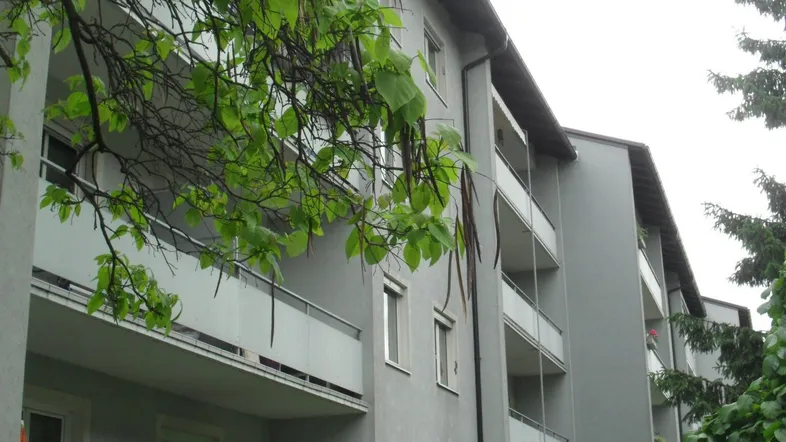 Mehrfamilienhaus mit mehreren Balkonen und grüner Umgebung, umgeben von Bäumen.