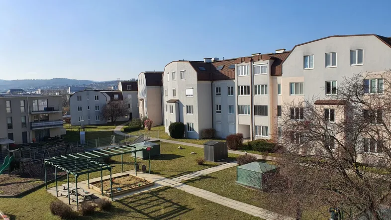 Blick von oben auf die Wohnanlage mit Gemeinschaftsgarten und Spielplatz unter blauem Himmel.