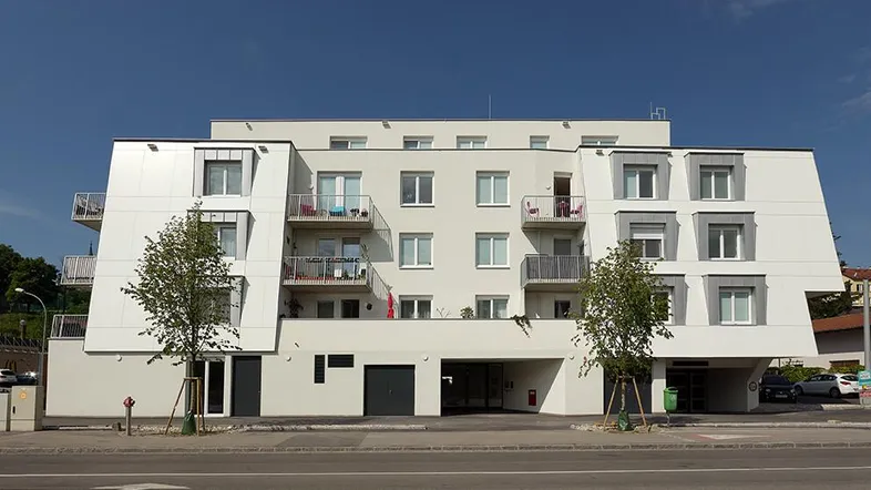 Moderne Wohnanlage mit weißer Fassade, Balkonen und großen Fenstern an einer Straße gelegen.