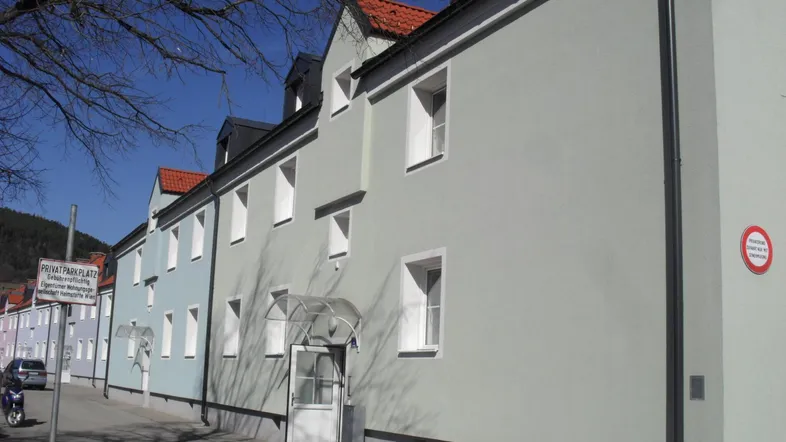 Reihenhausfassade in hellem Grau und Blau entlang einer Straße mit Privatparkplatzschild.