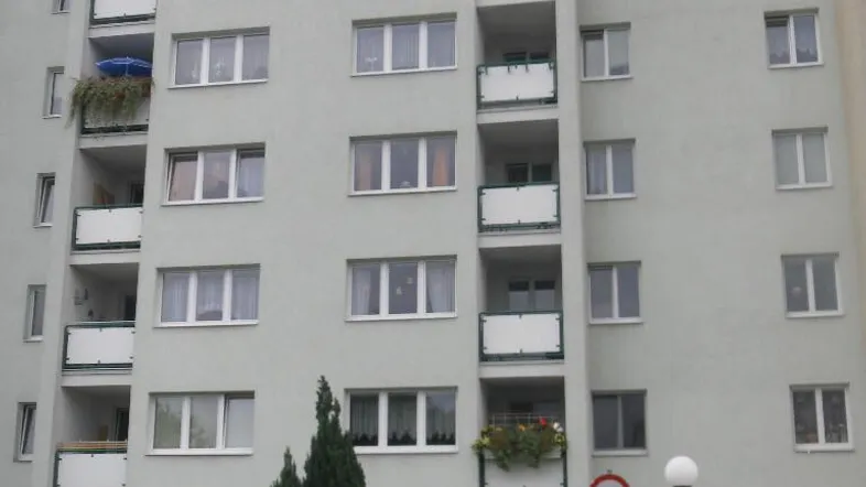 Ansicht eines Mehrfamilienhauses mit mehreren Balkonen und einer Grünfläche davor.