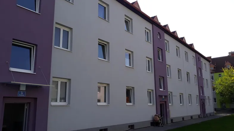 Ansicht eines Mehrfamilienhauses mit lila und grauer Fassade und gepflegtem Rasenbereich.