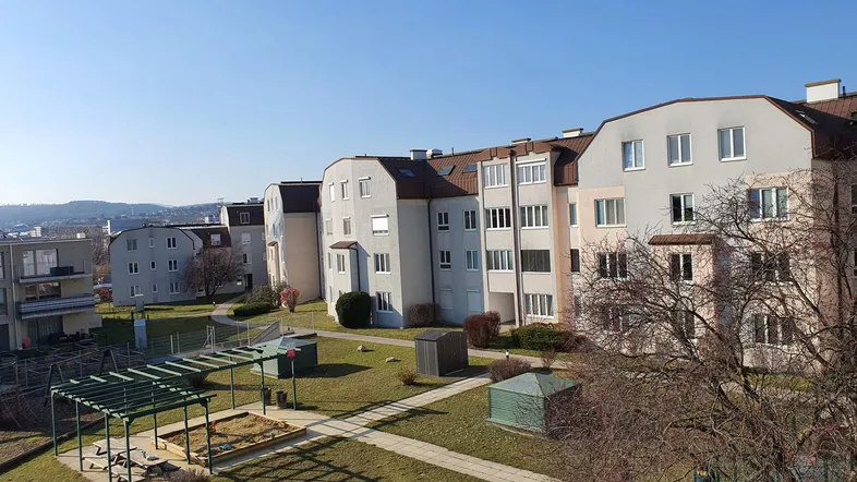Weitläufiger Innenhof mit mehreren Wohngebäuden, Grünflächen und einem Kinderspielplatz unter blauem Himmel.