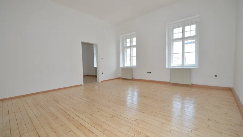 Heller, leerer Raum mit weiß gestrichenen Wänden, Holzdielenboden und zwei Fenstern.