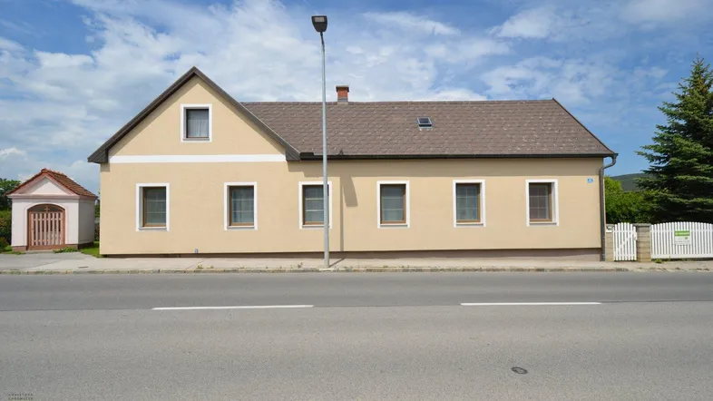 Traditionelles Einfamilienhaus mit beiger Fassade und Satteldach, direkt an einer Straße gelegen.