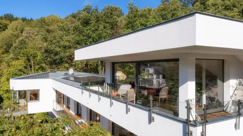 Moderne Architektur mit großzügigem Balkon und Glasgeländer, umgeben von üppiger Natur.
