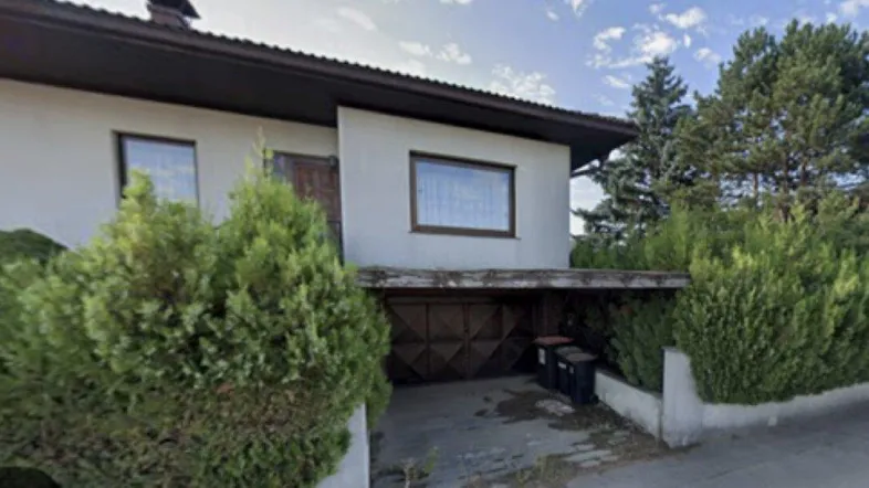 Einfamilienhaus mit Satteldach, Carport und gepflegter Hecke an der Straße.
