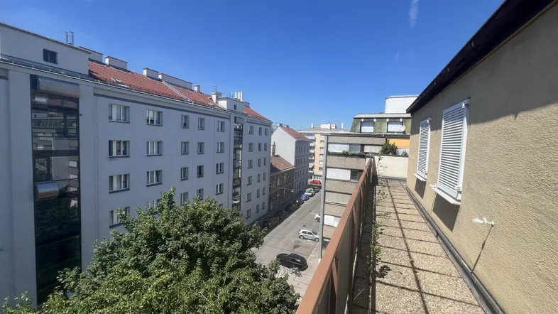 Geräumiger Balkon mit Blick auf die Stadt und umliegende Gebäude unter blauem Himmel.