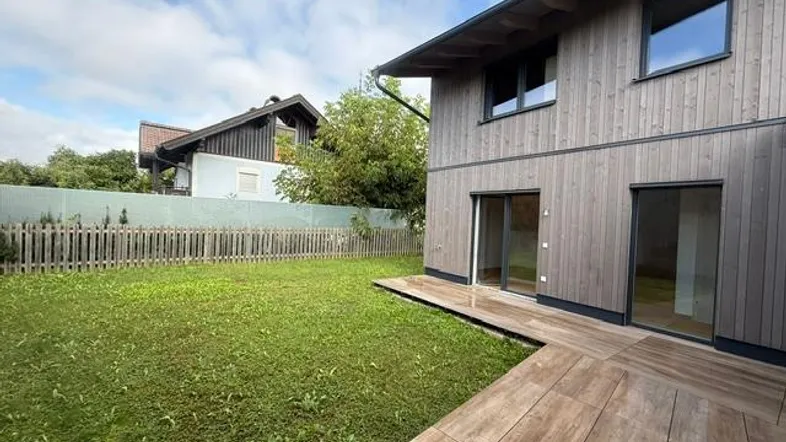 Moderne Holzfassade mit kleiner gefliester Terrasse und angrenzender Rasenfläche.