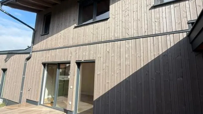 Moderne Holzfassade eines Hauses mit großer Terrasse und Blick auf den blauen Himmel.