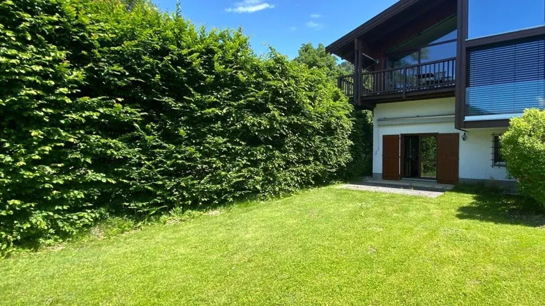 Grüner Gartenbereich mit gepflegtem Rasen und hoher Hecke neben dem Haus.