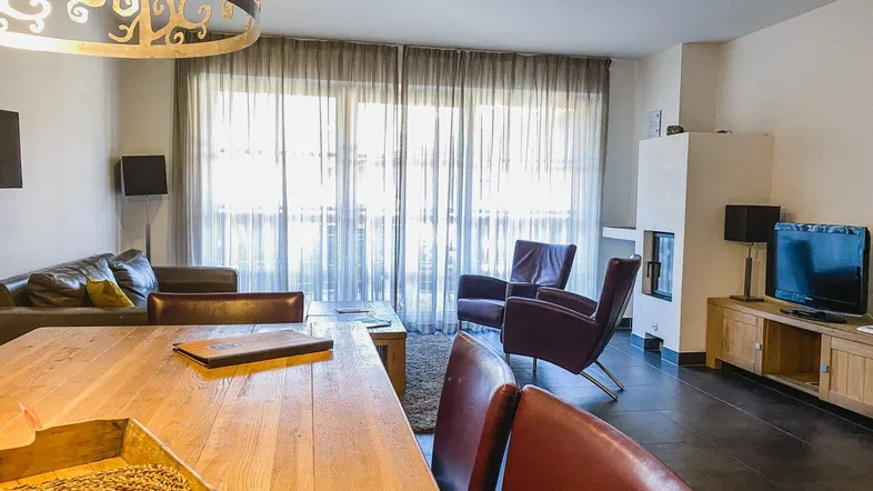 Geräumiger Wohn- und Essbereich mit Holztisch, bequemen Sofas und großen Fenstern mit Zugang zum Balkon.