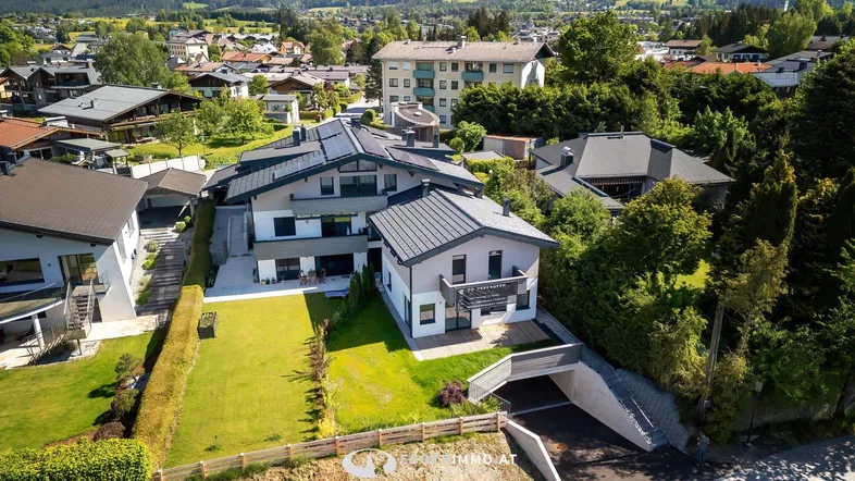 Luftaufnahme eines modernen Wohnkomplexes mit gepflegten Gärten und umliegender Bebauung.
