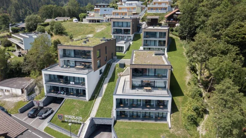 Moderne Apartmentgebäude mit Gründächern und Balkonen, eingebettet in eine Hanglage mit Bergblick.
