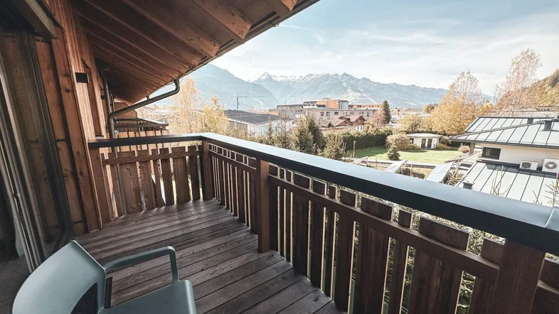 Geräumiger Holzbalkon mit Sitzgelegenheiten und weitem Blick auf die umliegende Berglandschaft.