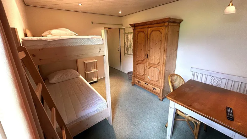 Gemütliches Schlafzimmer mit Etagenbett, Holzschrank und kleinem Esstisch für Gäste.
