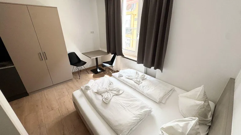 Helles Schlafzimmer mit Doppelbett, kleinem Esstisch und Kleiderschrank, ideal für ein Studio-Apartment.
