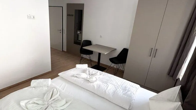 Helles Schlafzimmer mit Doppelbett, Kleiderschrank und kleinem Esstisch für zwei Personen.