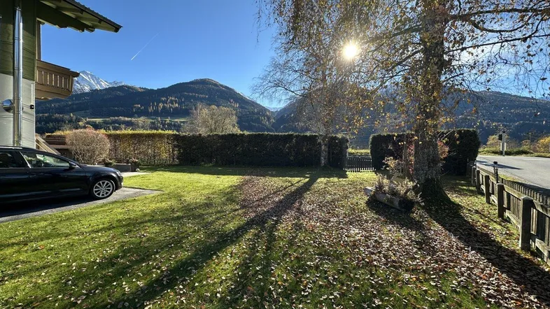 Sonnige Außenansicht des Hauses mit gepflegtem Rasen, Hecke und beeindruckendem Bergblick.