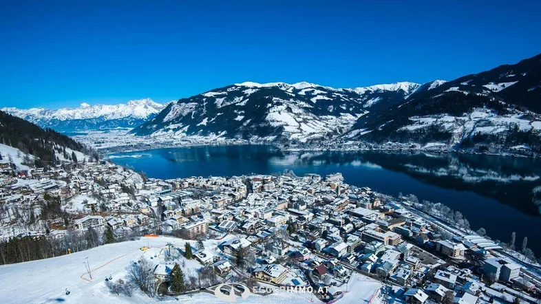 Panoramablick auf eine verschneite Stadt am See, umgeben von majestätischen Bergen im Winter.