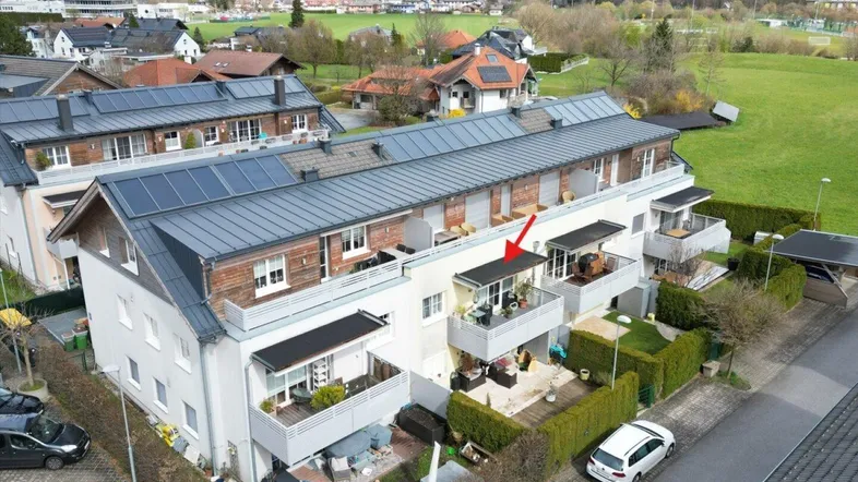 Luftaufnahme eines modernen Wohnkomplexes mit Balkonen, umgeben von grünen Wiesen und Bergen im Hintergrund.