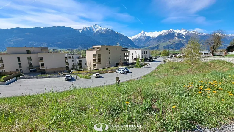 Panoramablick auf moderne Wohngebäude mit schneebedeckten Bergen im Hintergrund unter blauem Himmel.