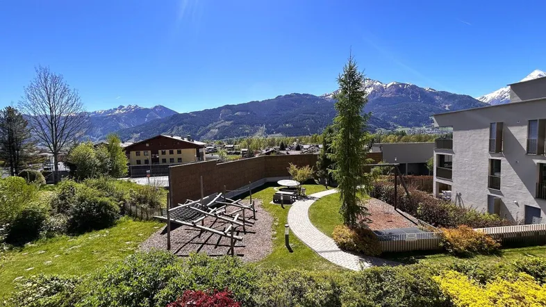Panoramablick auf die umliegende Berglandschaft mit Grünflächen und Wohngebäuden unter blauem Himmel.