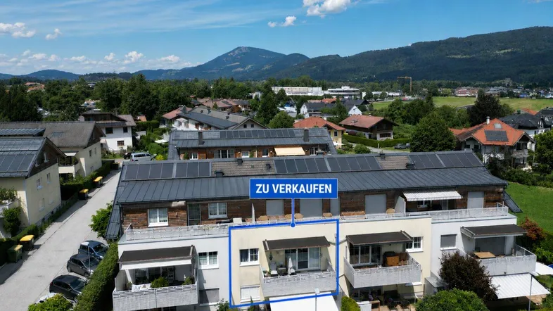 Luftaufnahme eines modernen Wohnkomplexes mit Balkonen und Bergblick, eine Einheit ist zum Verkauf markiert.