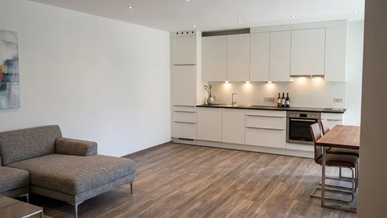 Heller offener Wohnbereich mit integrierter Küche, modernem Sofa und Laminatboden.