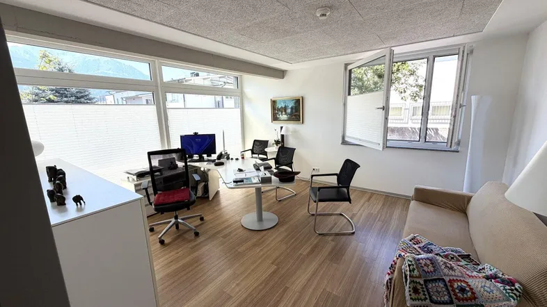 Geräumiges Büro mit großen Fenstern, Holzboden und Blick auf die Berge, ausgestattet mit mehreren Arbeitsplätzen und einer Couch.