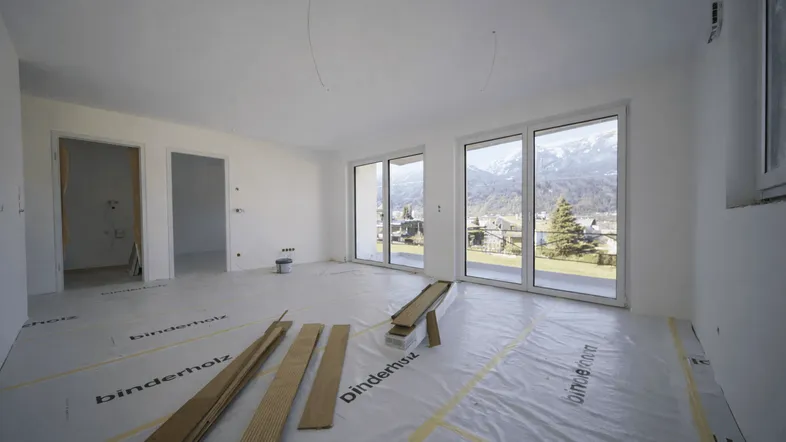 Geräumiger Wohnraum im Neubau mit vorbereitetem Boden für Holzdielen und Bergblick.