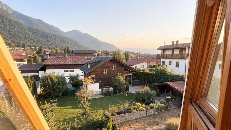 Panoramablick aus einem Fenster auf die umliegende Wohngegend mit Bergen im Hintergrund bei Sonnenuntergang.
