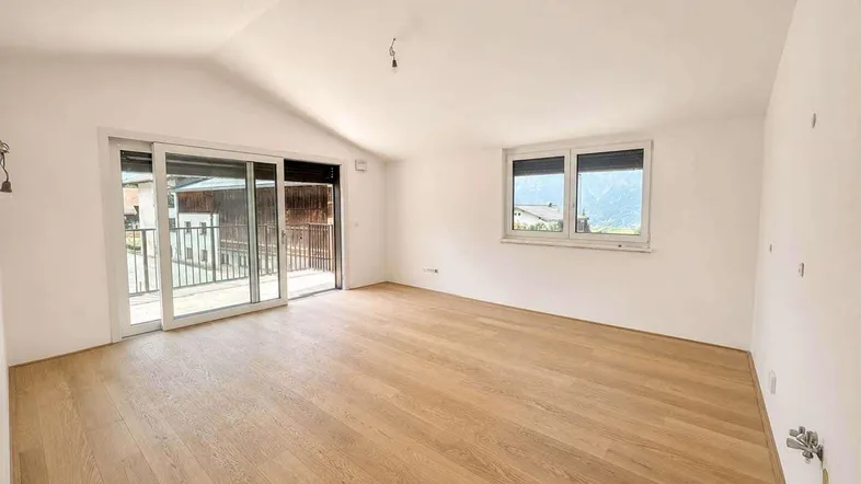 Helles Zimmer mit Holzboden, Schiebetür zum Balkon und weitem Bergblick.