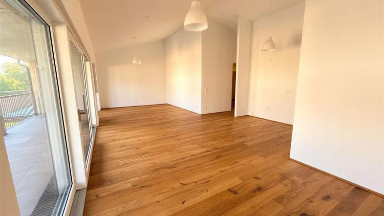 Helles Wohnzimmer mit Holzboden, weißen Wänden und Zugang zu einem Balkon.