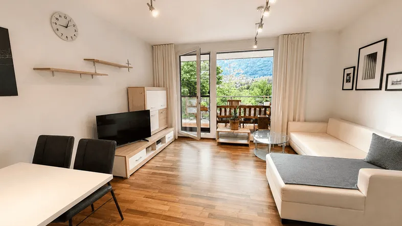 Helles Wohn- und Esszimmer mit Holzboden, Balkonzugang und weitem Bergblick.