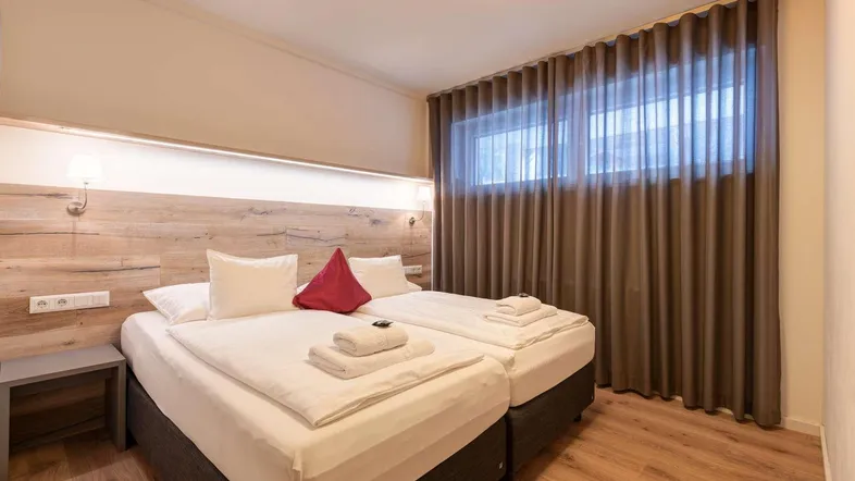 Gemütliches Schlafzimmer mit zwei Einzelbetten, Holzkopfteil und braunen Vorhängen.