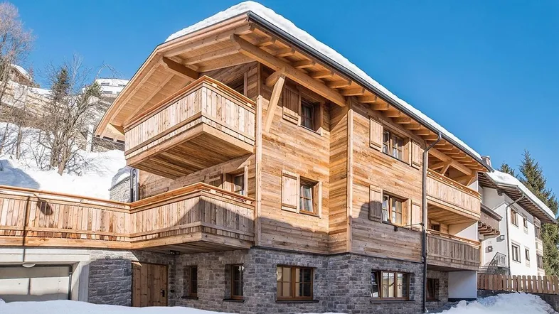 Traditionelles Holzchalet mit Steinsockel und schneebedecktem Dach in alpiner Umgebung.