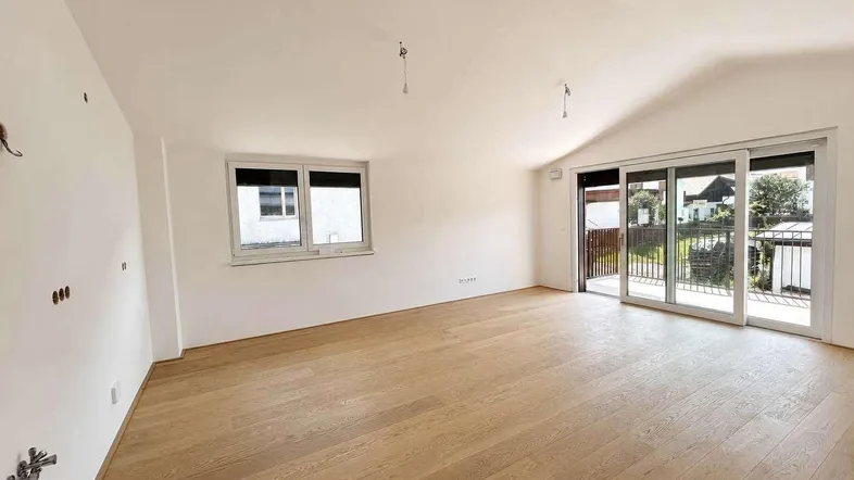 Helles Wohnzimmer mit Holzboden und Zugang zu einem Balkon, ideal für entspannte Stunden.