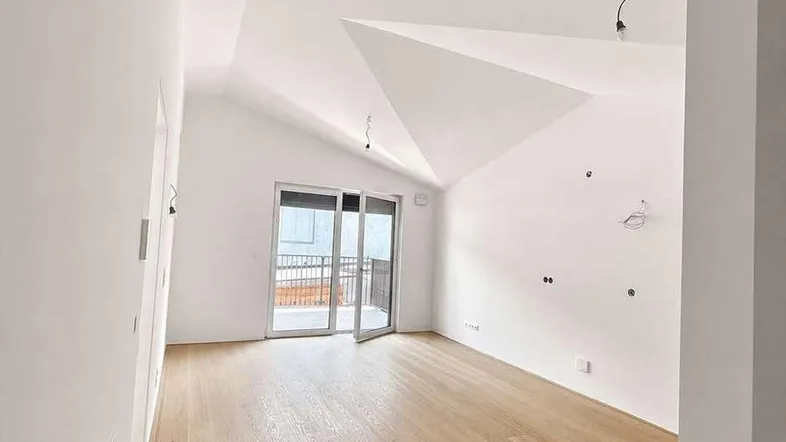 Helles Zimmer mit Holzboden, schrägen Decken und Zugang zu einem Balkon.